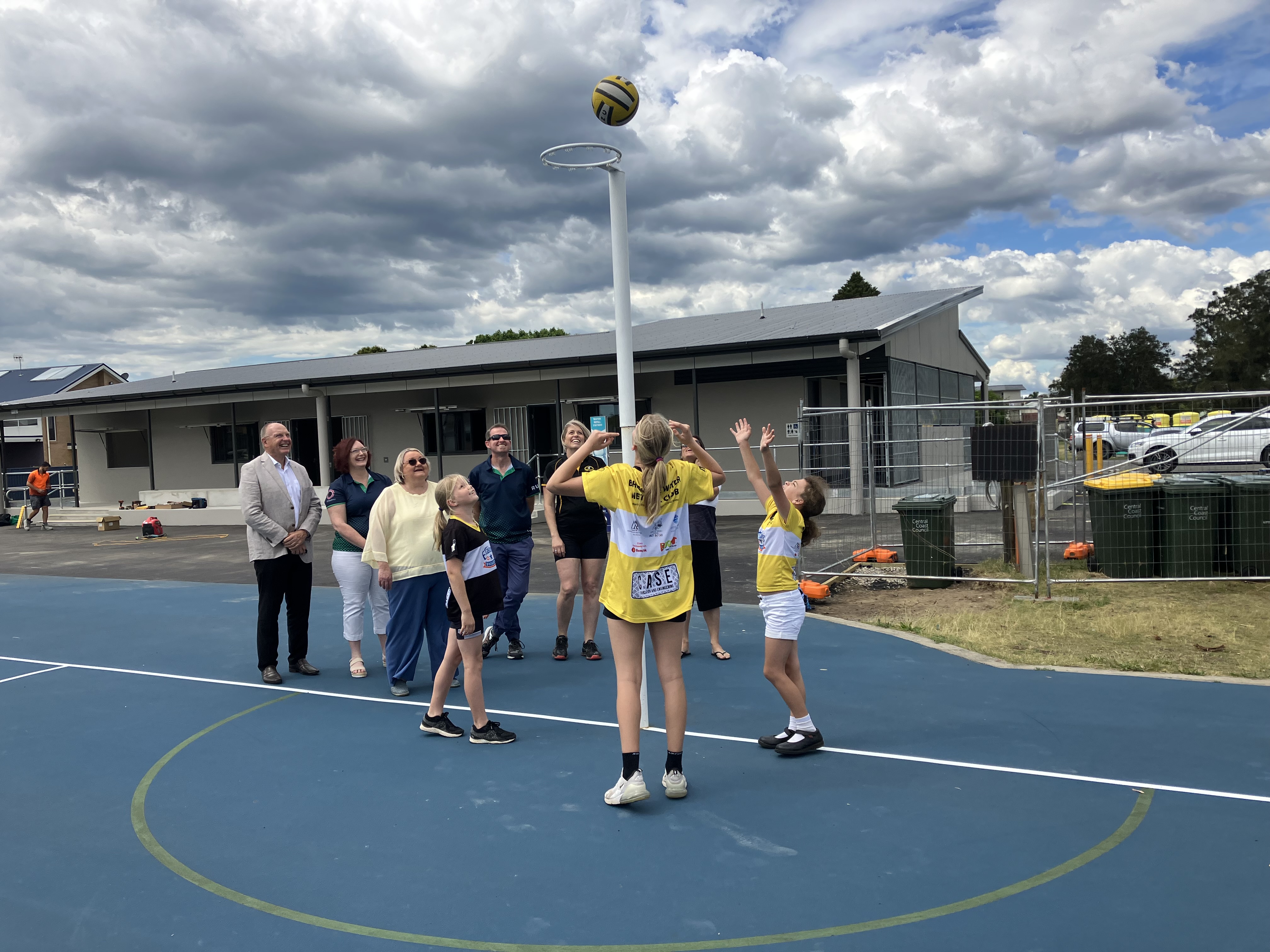 Girls playing netball with adults watching 