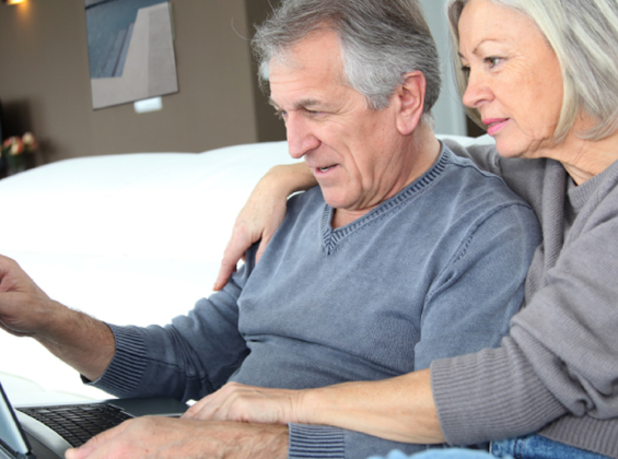 Older man and Woman sitting on couch looking at laptop