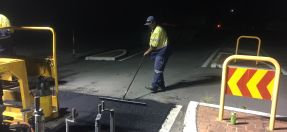 Heavy patching repairs roadworks - worker in high vis with machine and section of road being repaired at night